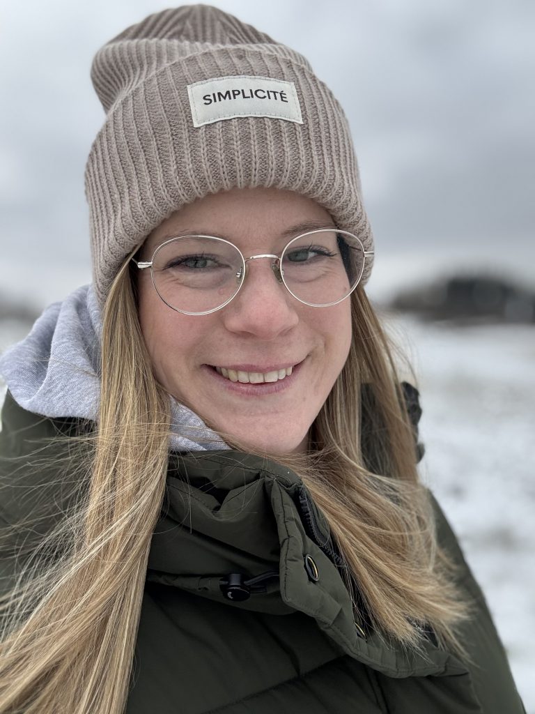 Karen mit dicker Mütze umgeben von Schneelandschaft.