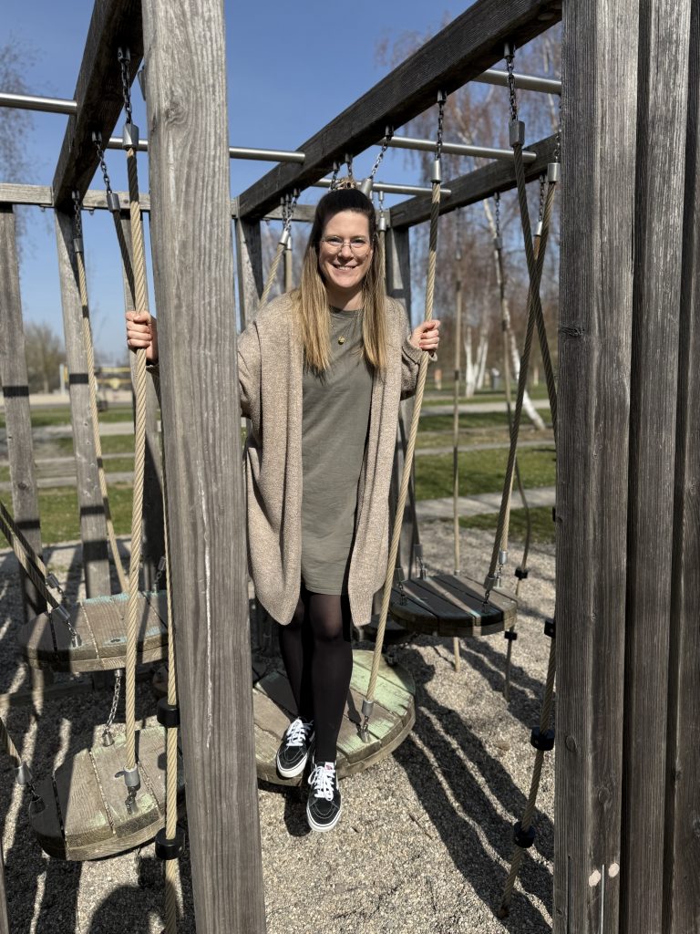 Karen auf einem Klettergerät zwischen Baumstämmen.