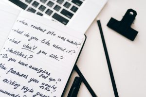Eine Nahaufnahme von einem Notizbuch mit handgeschriebenen Notitzen und ein Laptop.