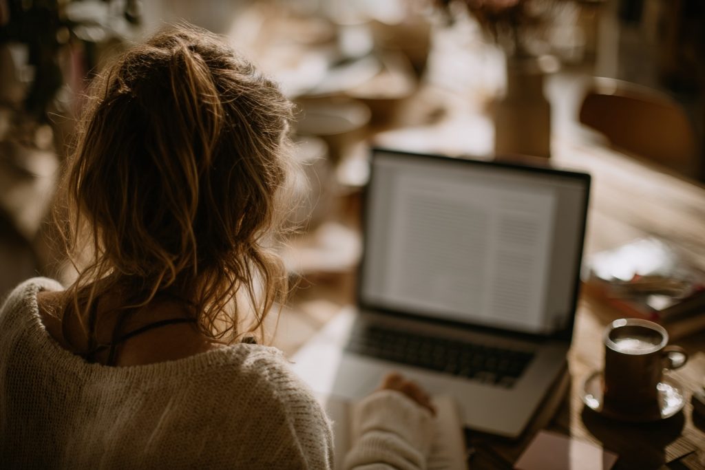 Blick über die Schulter einer Frau, die am Laptop sitzt und ihren Blogartikel oder Website-Texte selber schreibt. 