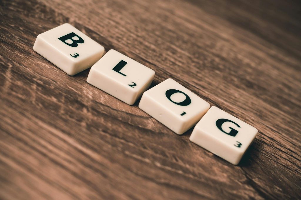 Scrabble Buchstaben, die das Wort "BLOG" schreiben auf einem hölzernen Hintergrund.